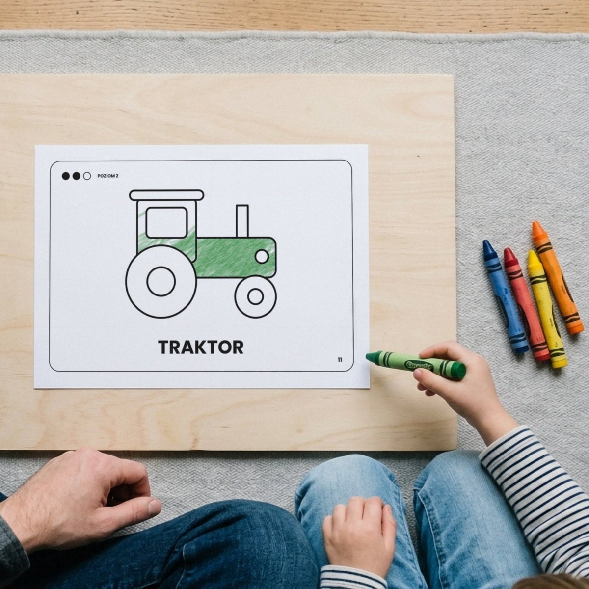 Dziecko koloruje zieloną kredką traktor z kolorowanki Pojazdy, obok siedzi dorosły